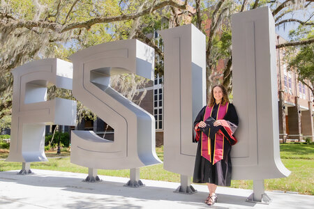FSU graduate in regalia leaning against FSU sign